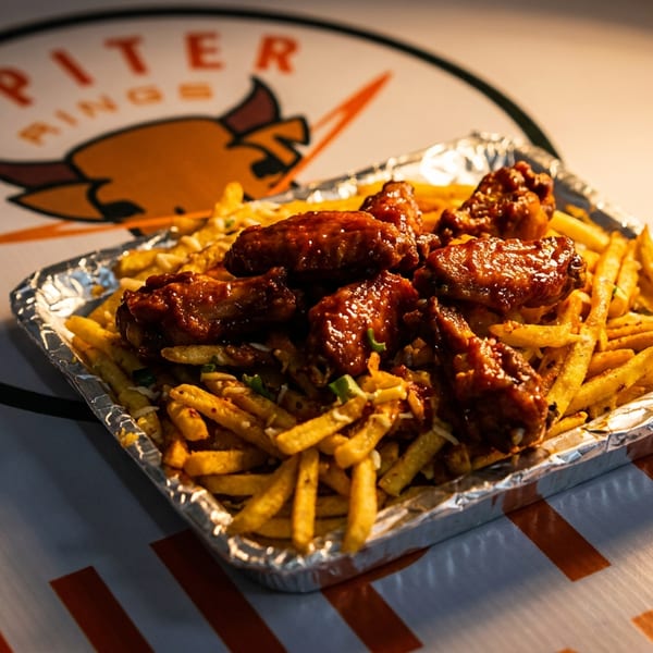 Saucy chicken wings and seasoned fries in a foil tray on a Jupiter Rings branded surface.